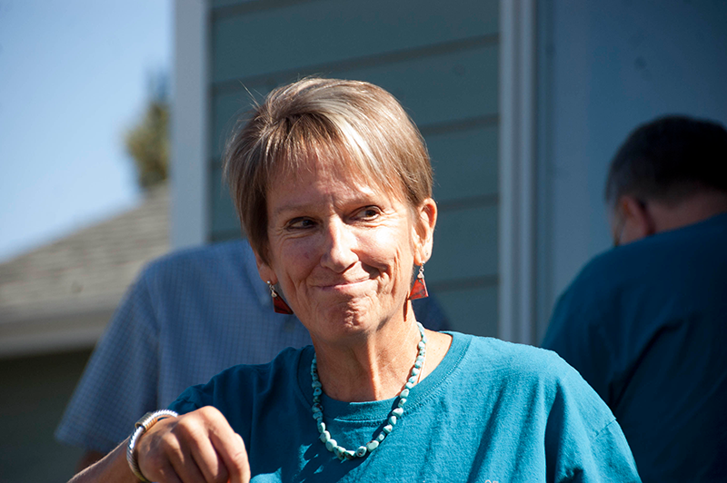 A woman in blue shirt and necklace smiling.